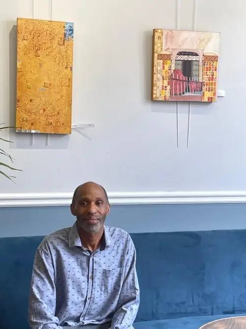 raymond isaac sitting in the southgate art gallery under two of his artworks 1