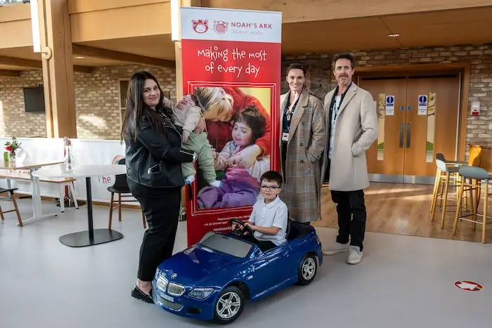 James Murray and Sarah Parish inside the hospice talking to Christiina Lucas-Dodsworth, who is holding her young child Arthur while Joseph Dodsworth sits in a toy car